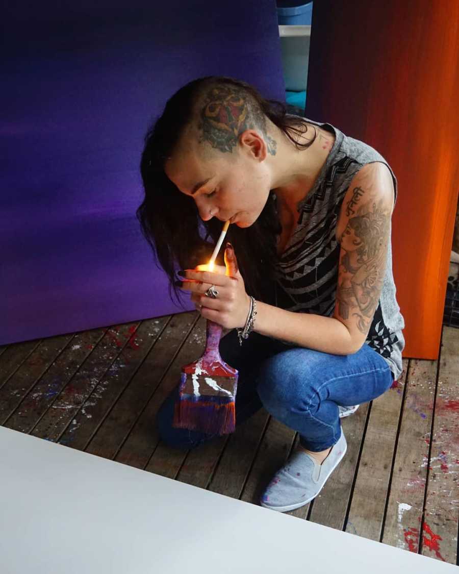 Woman with depression with half shaved head kneels while she lights a cigarette