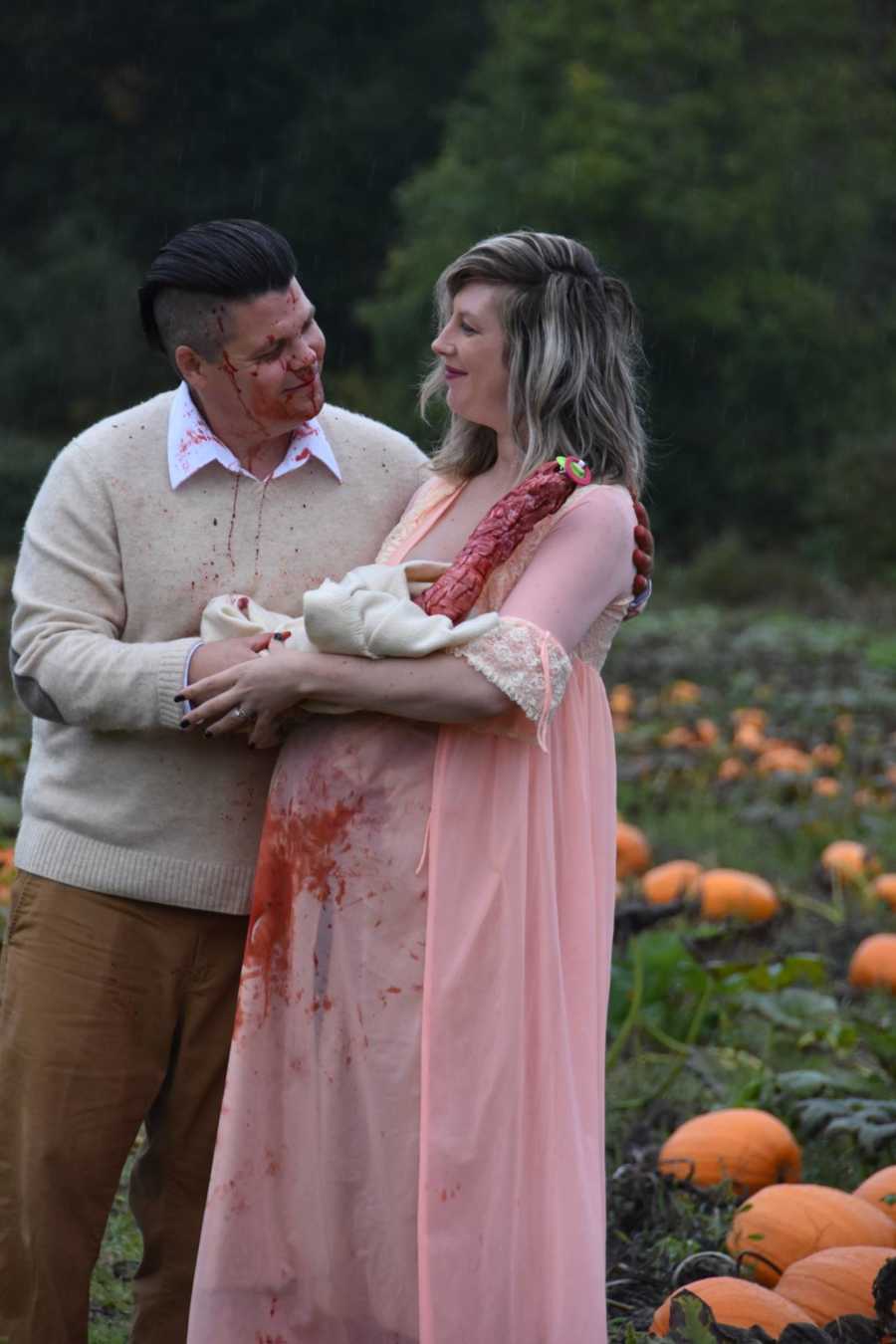 Husband and wife hold swaddled bloody creature that came out of wife's stomach in pumpkin patch