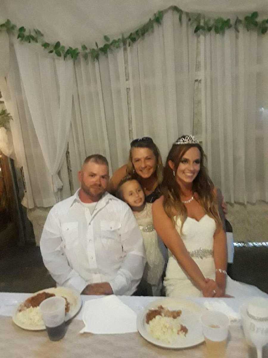 Bride and groom sit at table of wedding reception with daughter and bride's stepdaughter