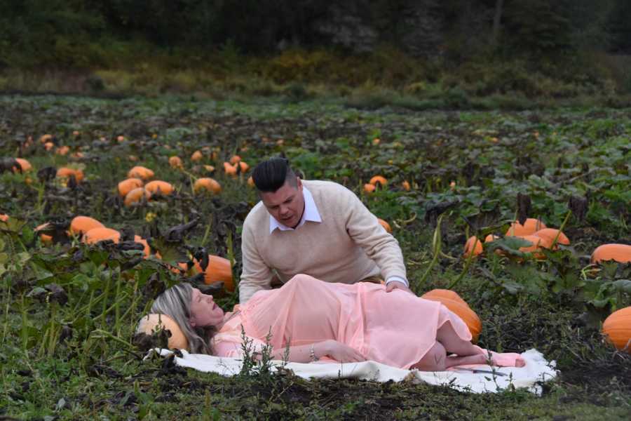Pregnant woman lays down on blanket in pumpkin patch in pain while husband sits beside her