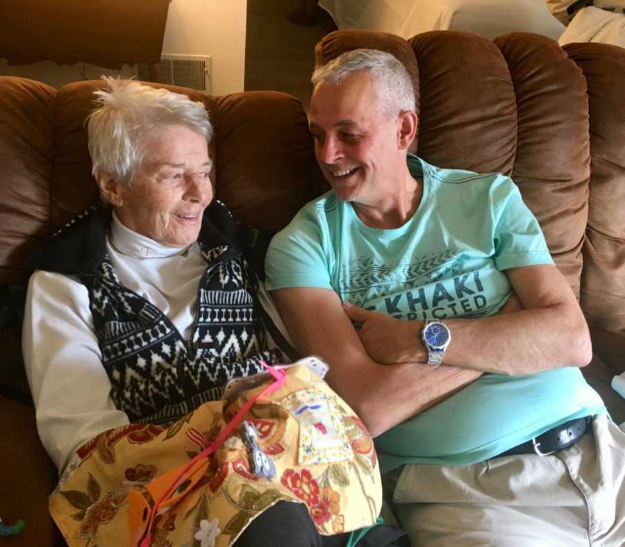 Elderly woman with dementia sits on couch beside man who was her foreign exchange student as a teen 