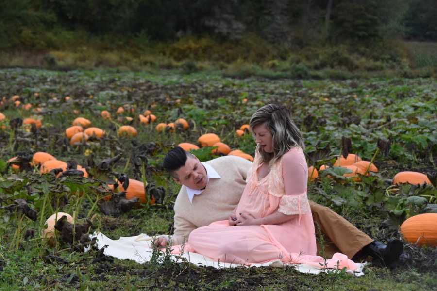 Pregnant woman holds stomach in pain while sitting beside husband on blanket in pumpkin patch