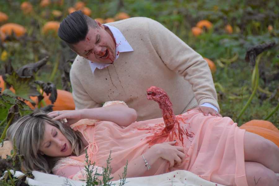 Woman lays in pumpkin patch while bloody monster comes out of her stomach and husband is covered in blood
