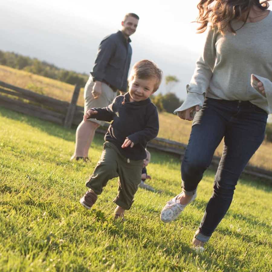 Mother runs beside son who running outside while father watches in background