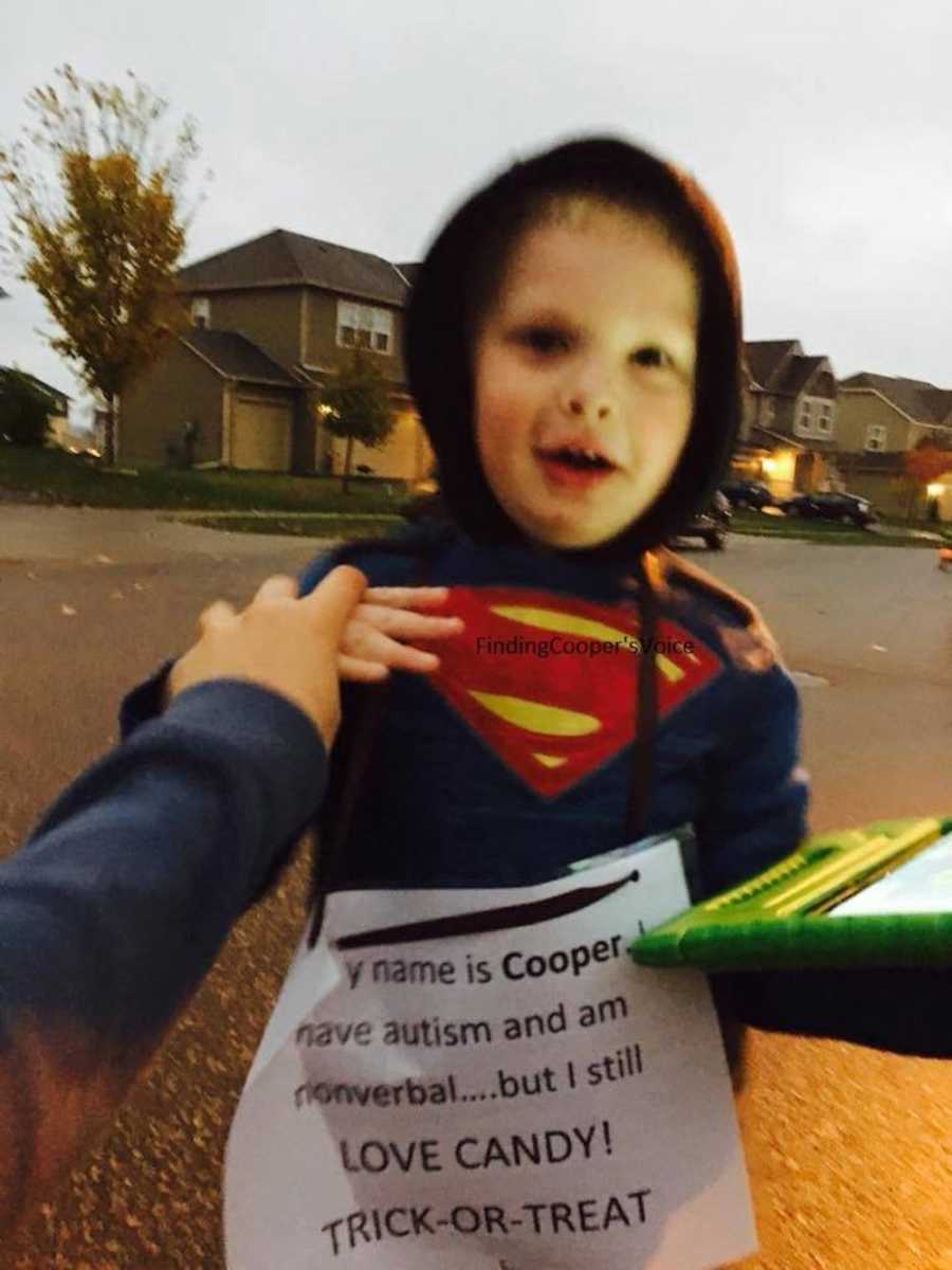 Young boy dressed as superman stands with sign on his chest that says, "My name is Cooper. I have autism..."
