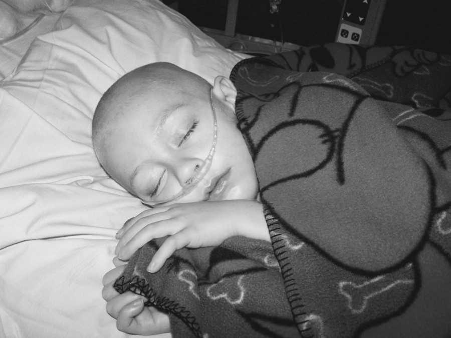 Young boy with cancer asleep in hospital bed with an oxygen tube up his nose