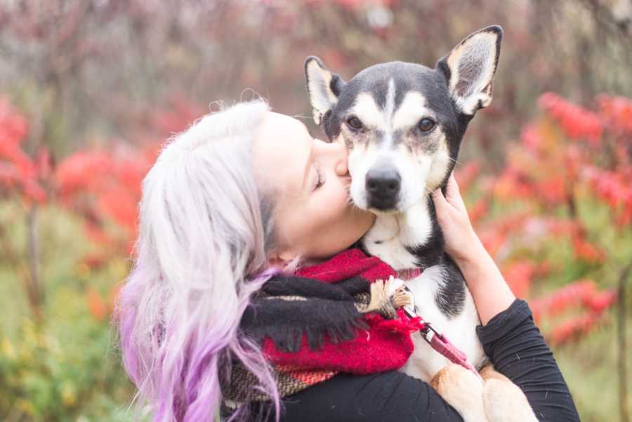 Woman kisses her dog as she holds him outside
