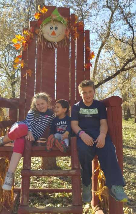 Three siblings sitting in Large red chair that has a scare crow and leaves on it