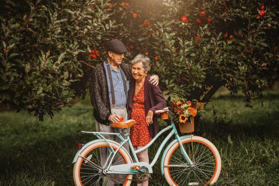 Elderly husband stands with arm around wife beside bike
