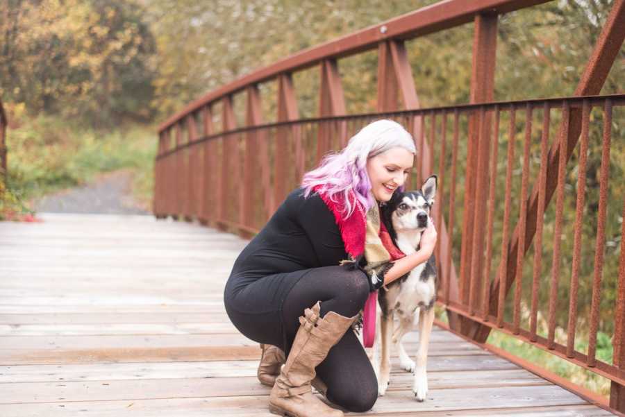 Woman kneels on bridge with arms wrapped around her adopted dog