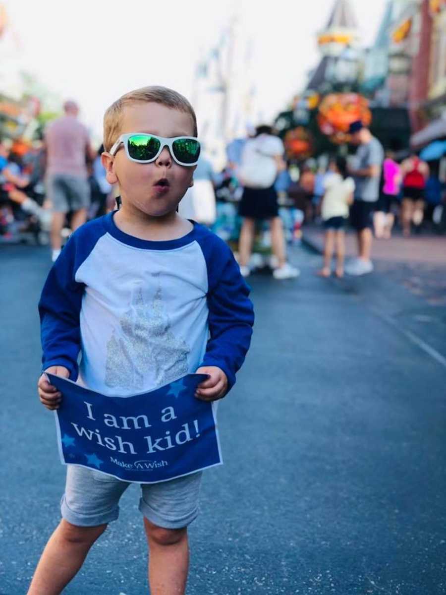 Little boy wearing sunglasses holding sign at Disney World that says, "I am a wish kid"