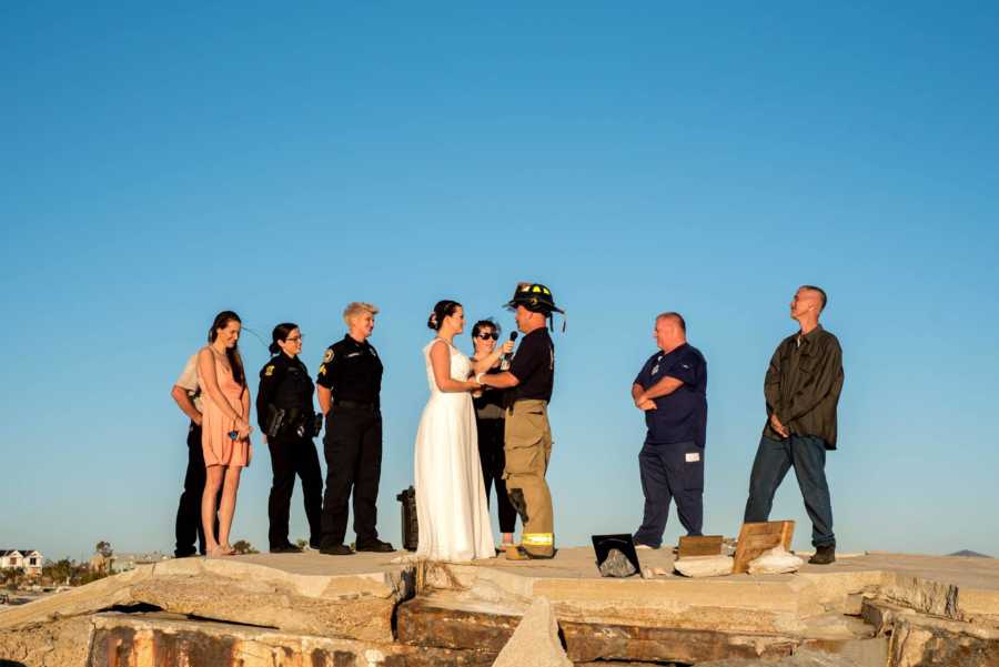Bride and fireman groom hold hands at outdoor wedding 