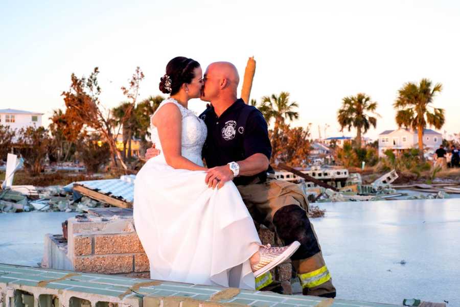 Bride and groom kiss while sitting on destruction from Hurricane Michael near body of water