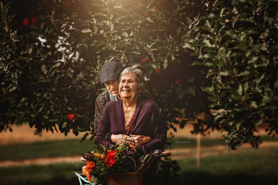 Elderly wife smiles as her husband stands behind her hugging her