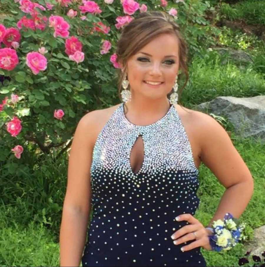 Teen smiling in prom dress with hand on her hip outside in front of pink flowers