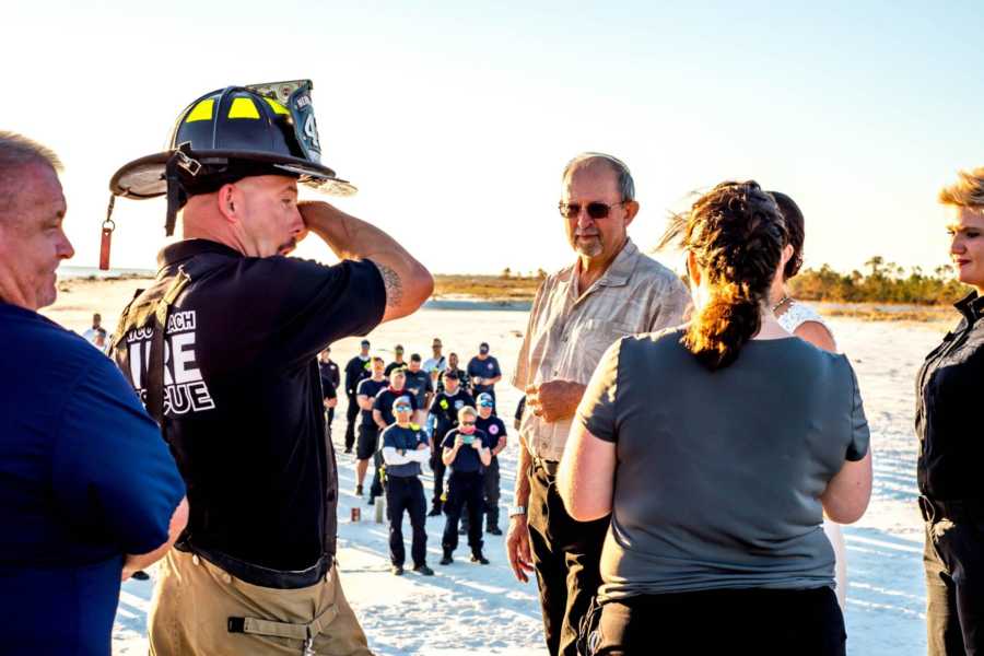 Fireman groom stands wiping tear at wedding outside with people watching