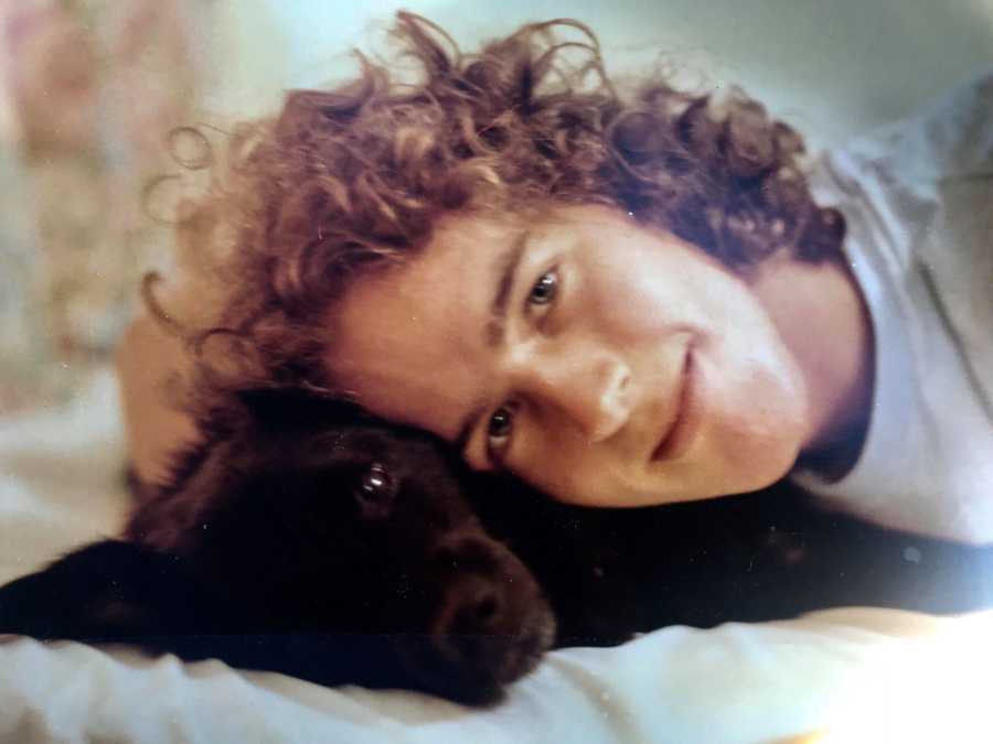 Man smiles as he rests head on dog lying down