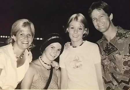 Ex husband and wife stand smiling with their two teen daughters standing between them