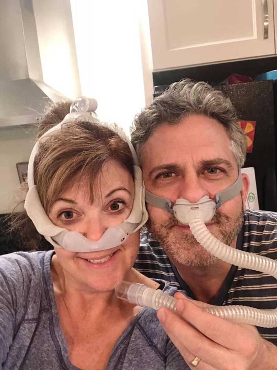 Husband and wife smile in selfie with sleep apnea machine on their face