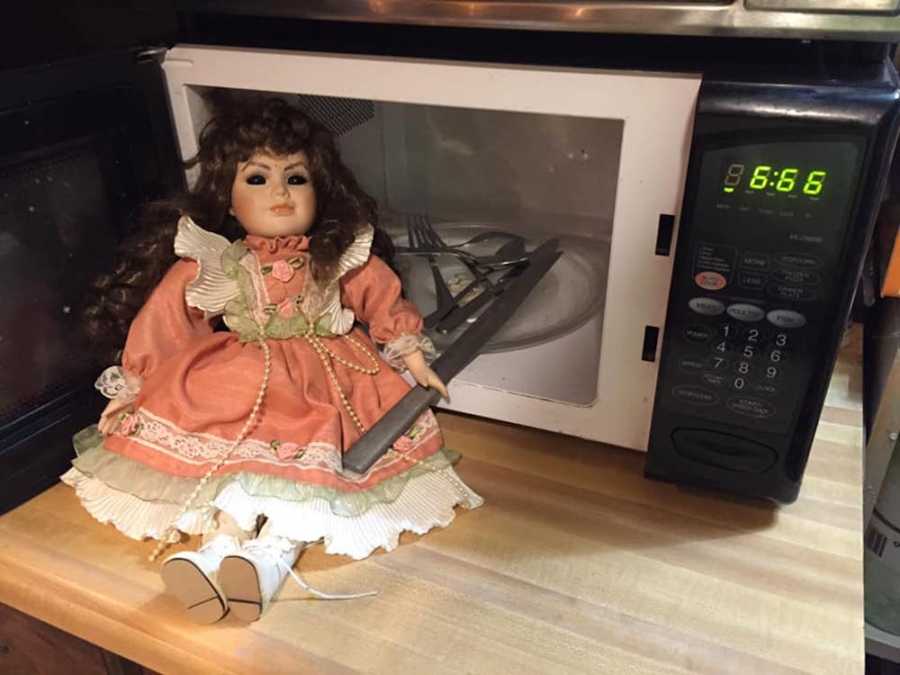 Doll leaning against open microwave door with silverware inside