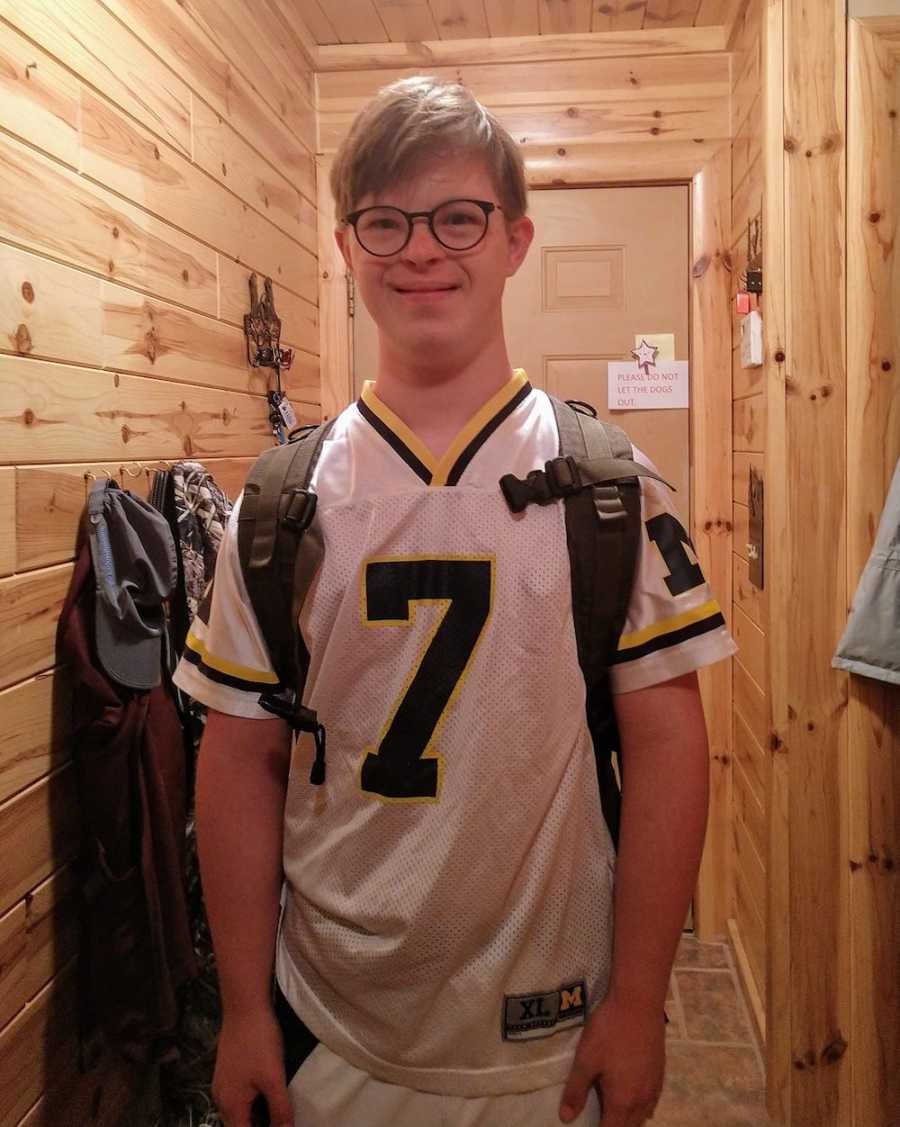 Teen with down syndrome stands smiling with jersey and backpack on