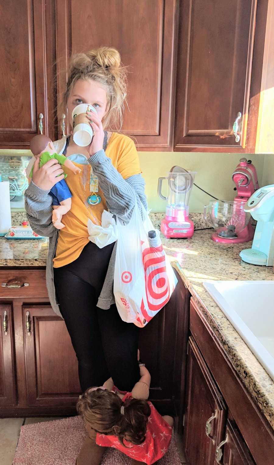 Teen dressed as "tired mom" stands in kitchen drinking out of Starbucks cup