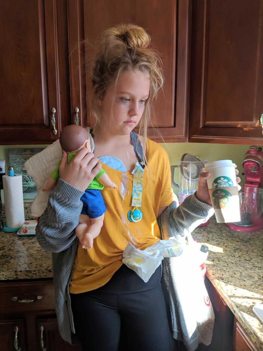 Teen dressed as "tired mom" stands in kitchen with stains on her shirt and dark circles under her eyes