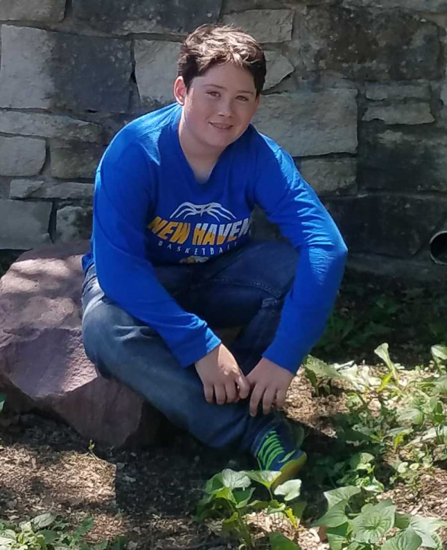 10 year old who attempted to commit suicide smiles as he sits on rock outside