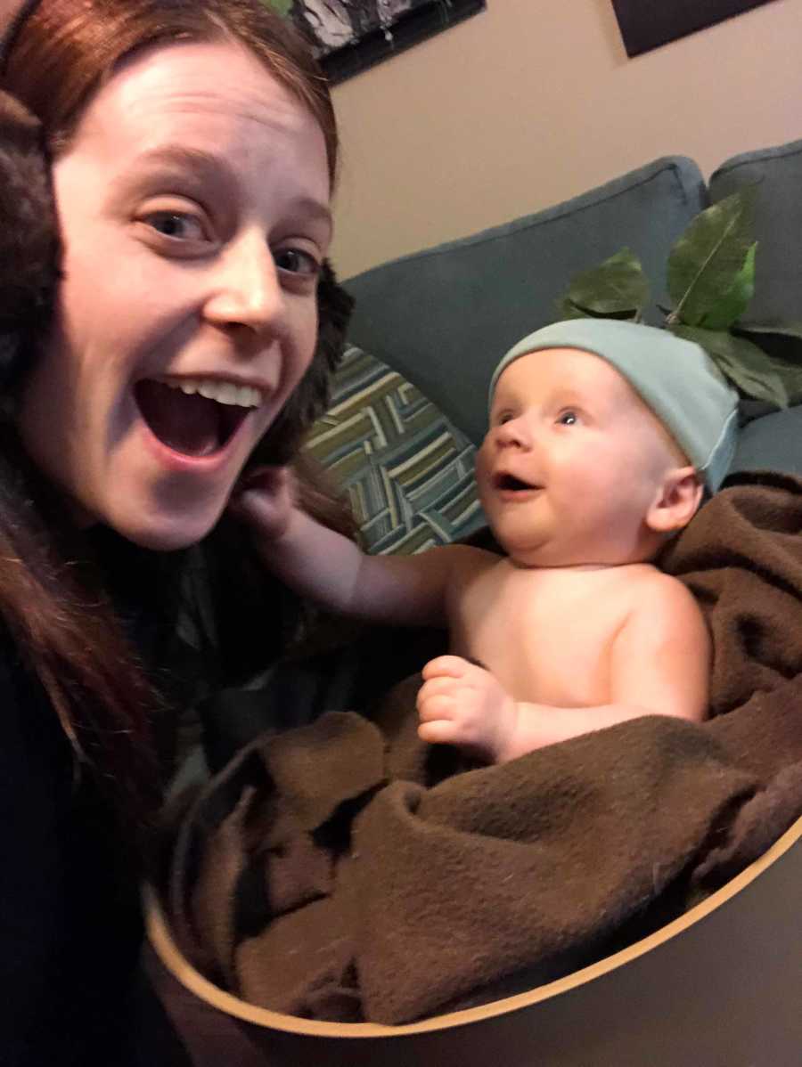 Mother wearing earmuffs smiles with mouth open as she takes selfie with son dressed as mandrake from Harry Potter