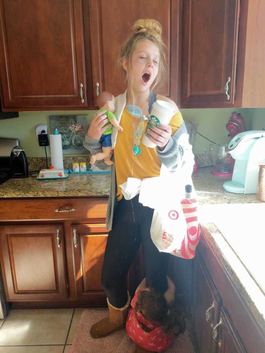 Teen dressed as "tired mom" stands yawning in kitchen