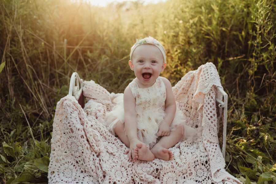 Young girl smiles as she sits on blanket in field for photoshoot