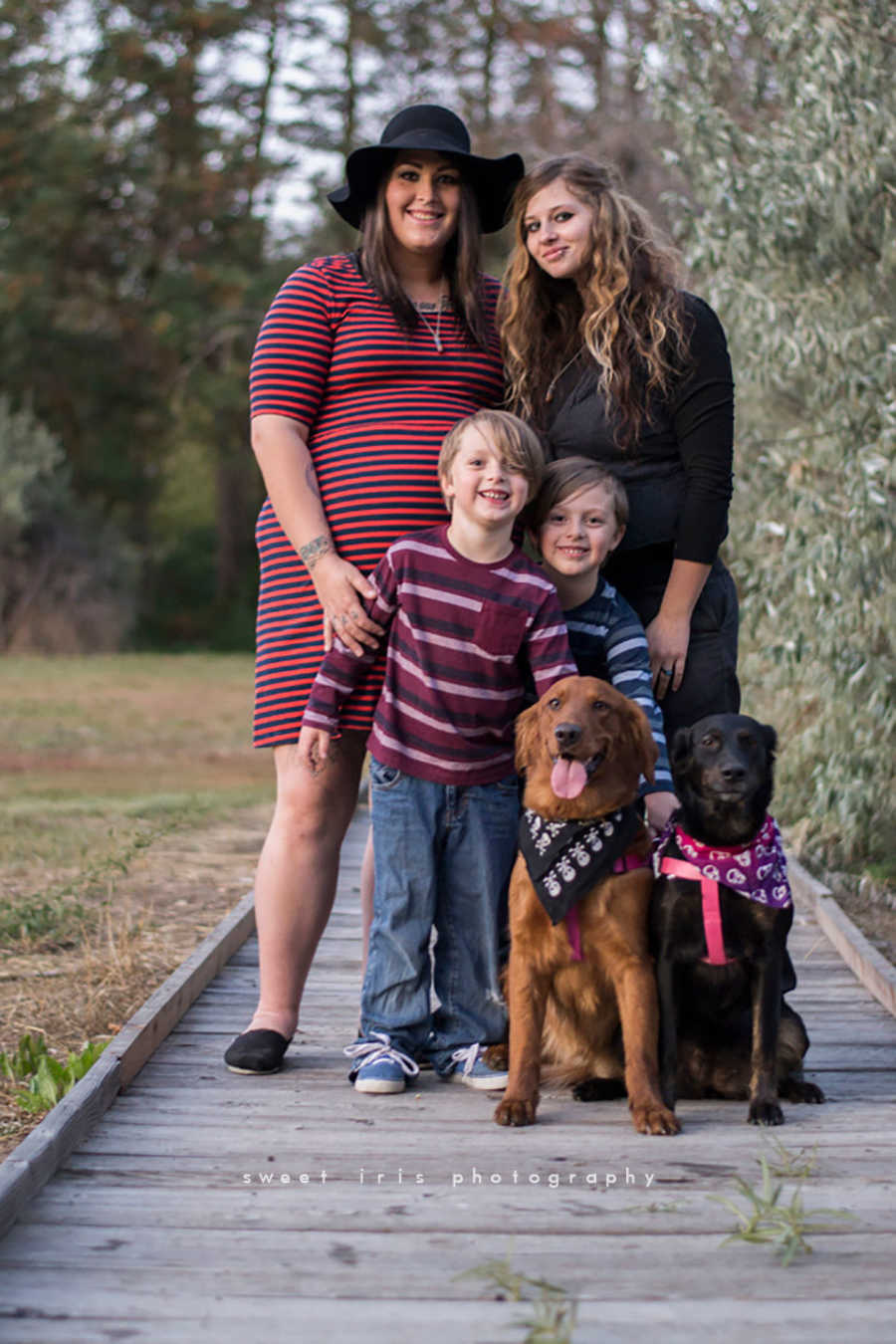 Same sex fiancee's stand smiling behind one of the woman's twin boys and two dogs