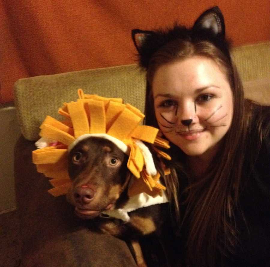 Woman dressed as a cat smiles in selfie with dog that has lion's mane on