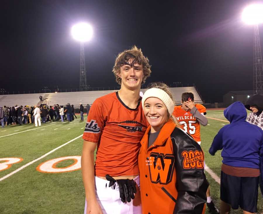 Teen football player stands smiling on field with cheerleader girlfriend after game
