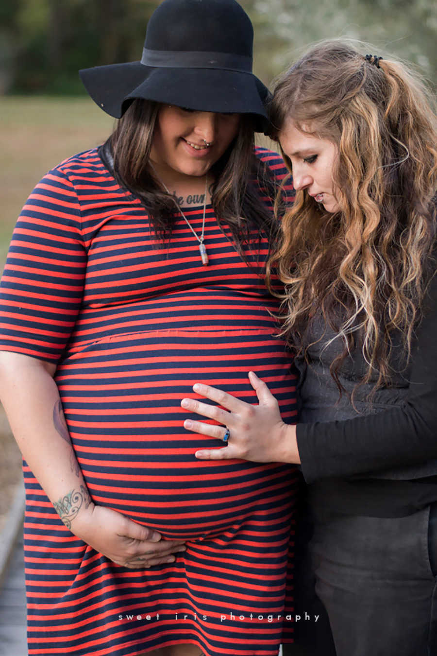 Pregnant woman looks down at her stomach while wife holds it