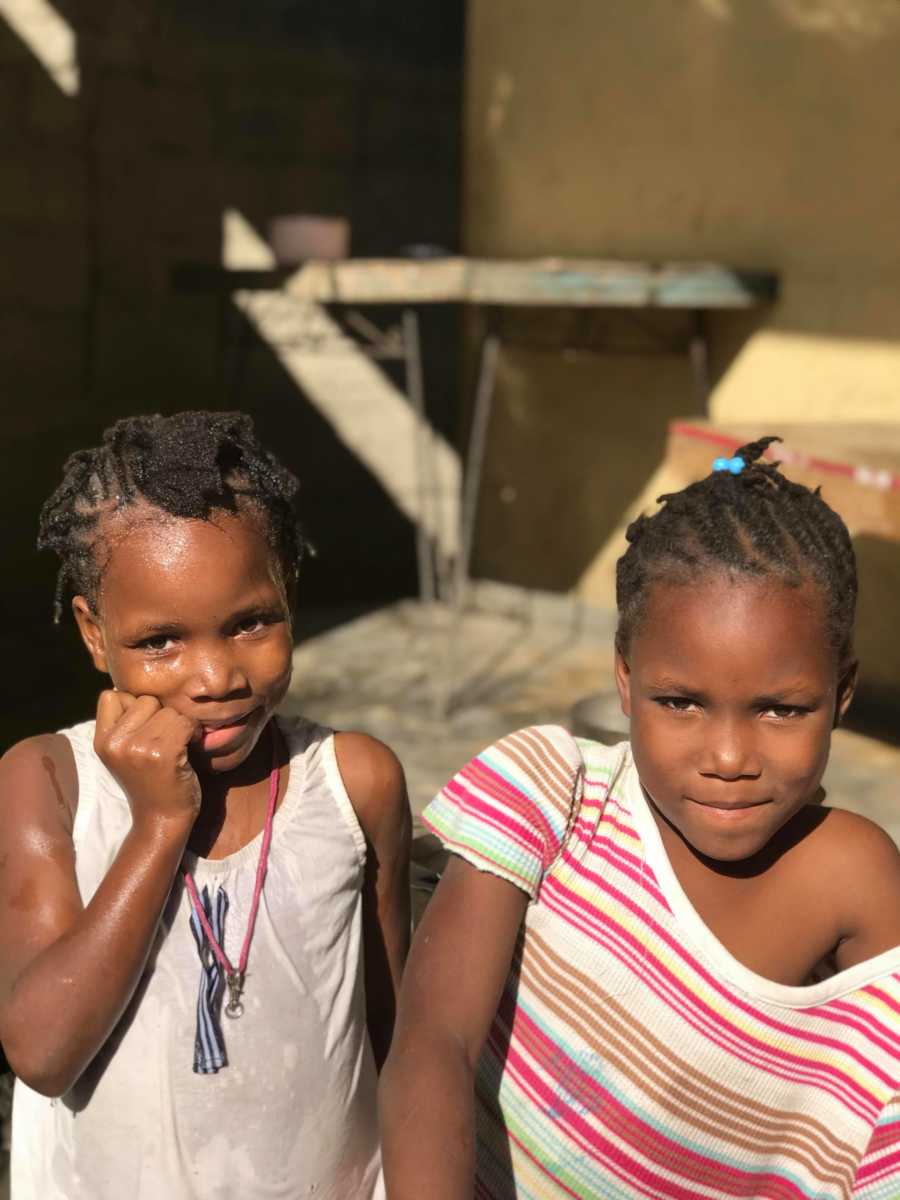 Two young foster girls in Haiti stands with smiles