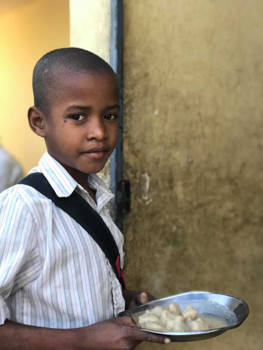 Young Haitian orphan stands holding plate of food