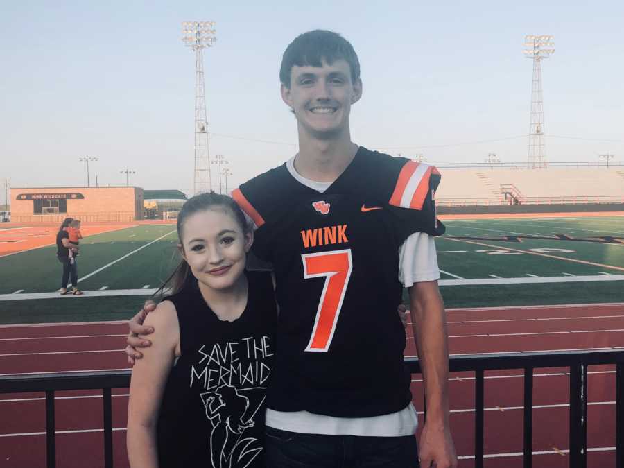 Teen stands in football jersey with arm around younger sister with chronic appendicitis