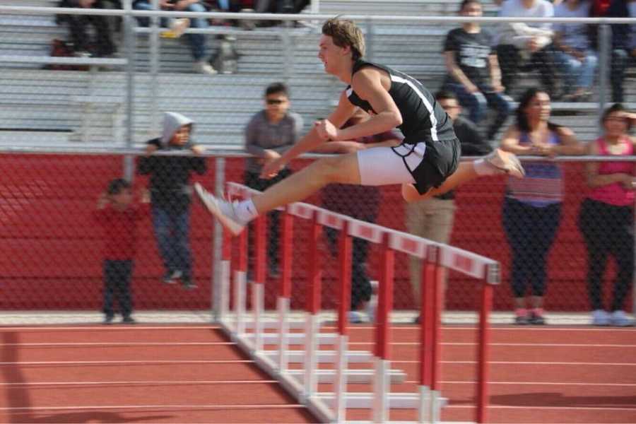 Teen jumping over hurdle in high school track meet