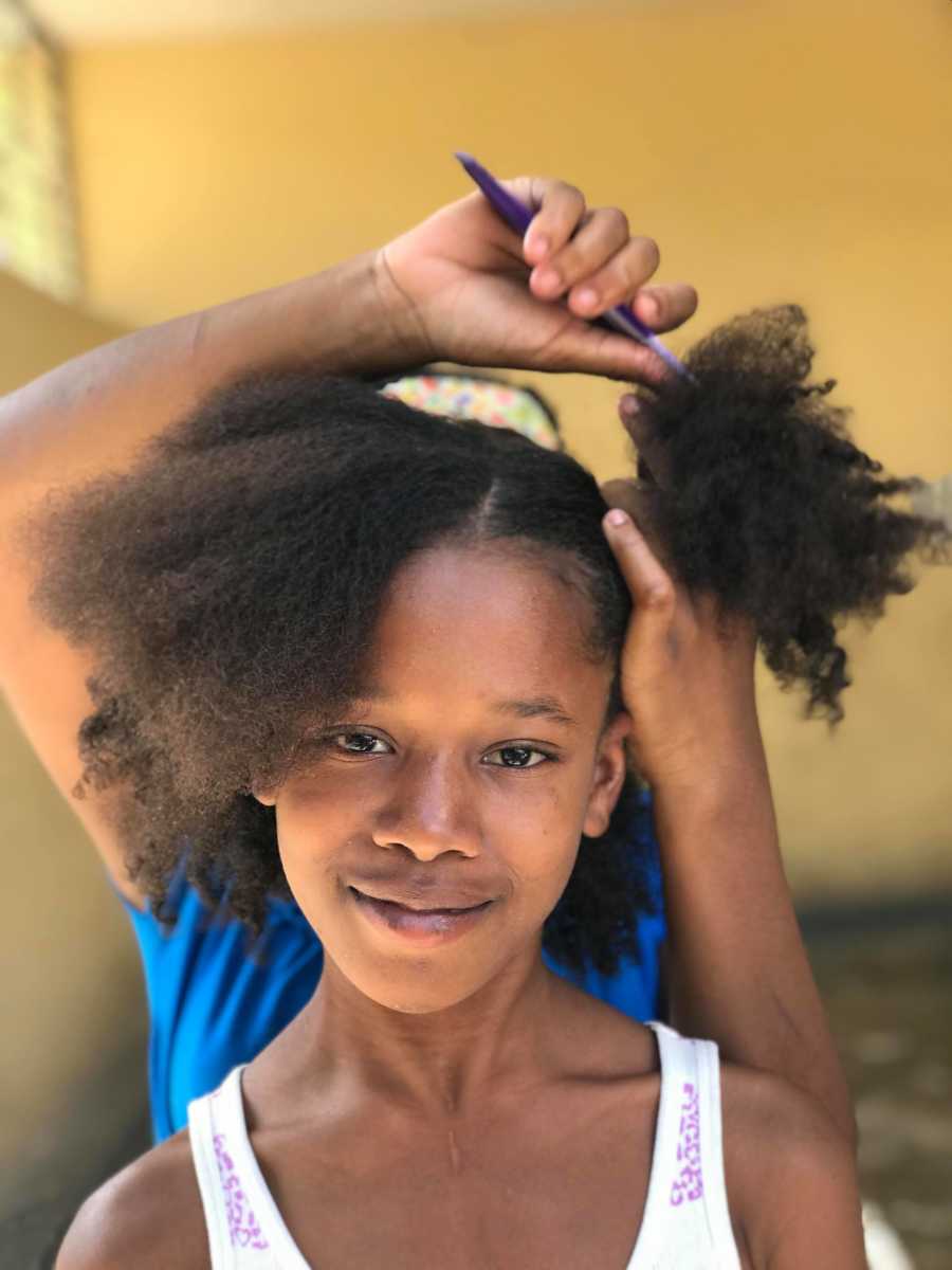 Haitian orphan smiles as someone behind her does her hair