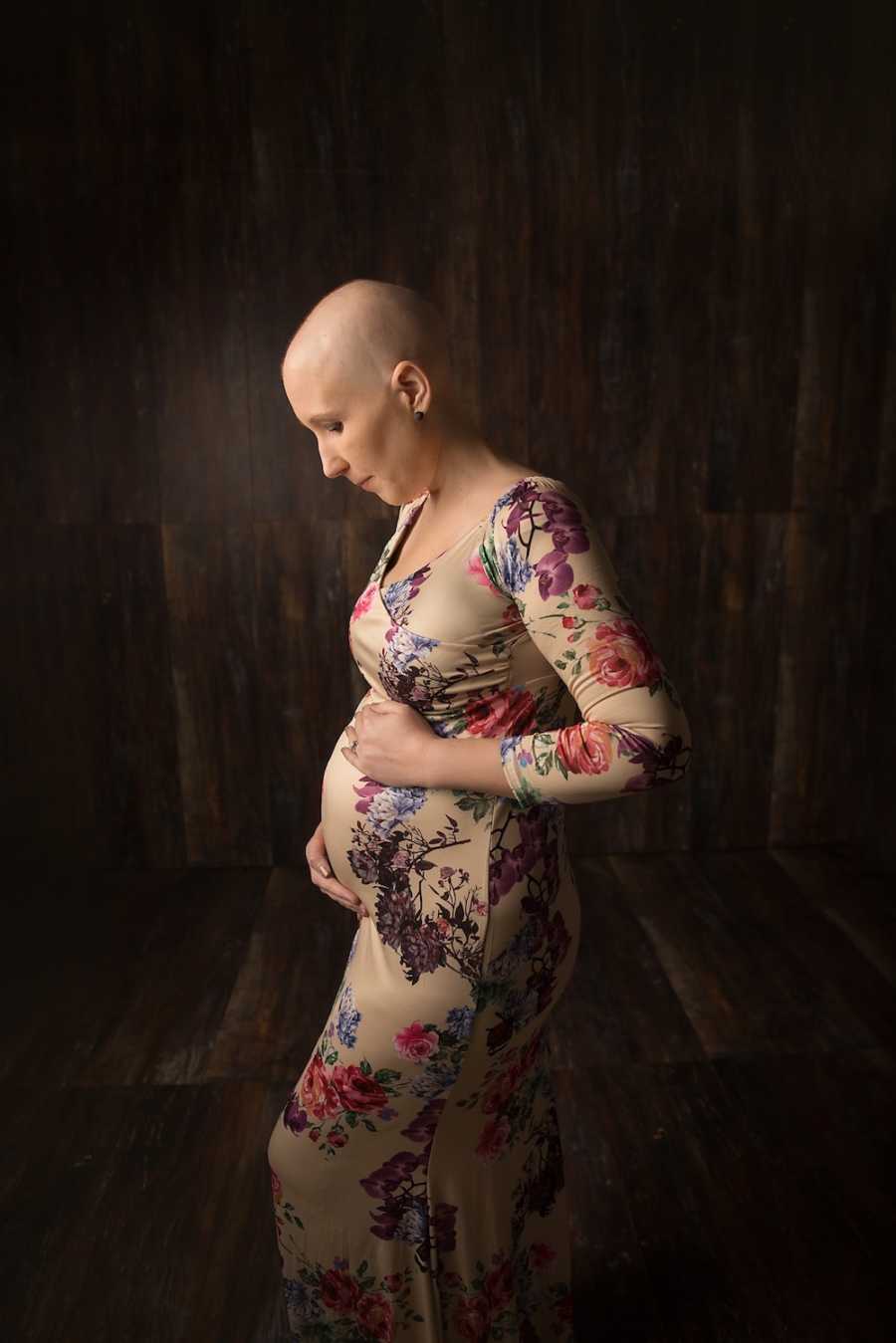 Woman with breast cancer stands holding her stomach in floral dress