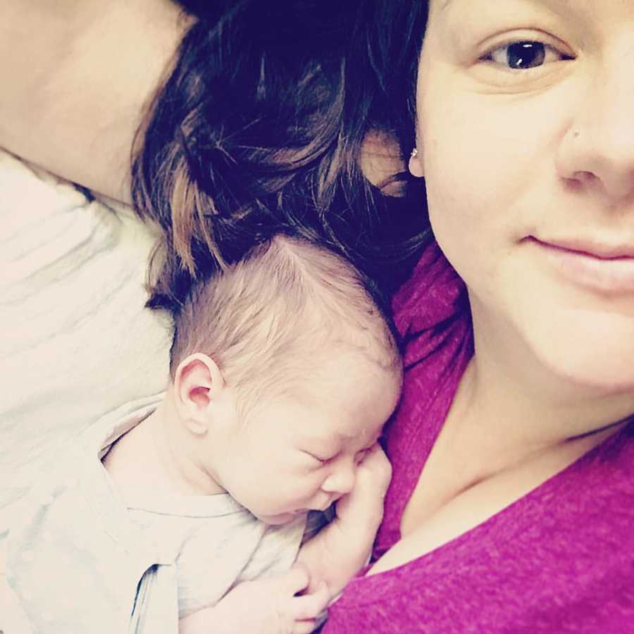 Mother smiles in selfie while her baby sleeps on her chest