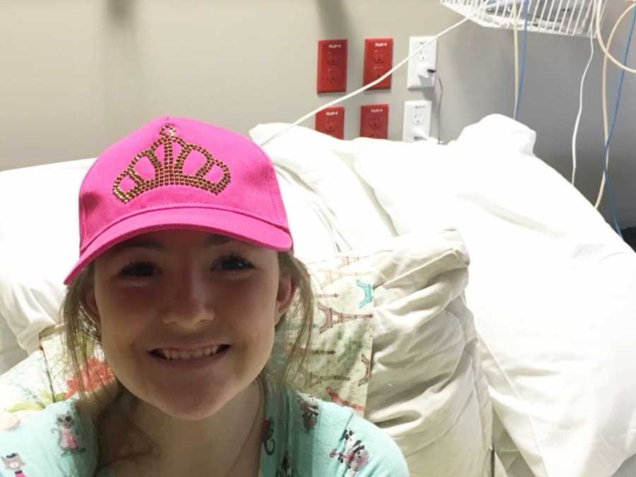 Ten year old with chronic appendicitis sitting in hospital bed wearing pink hat that had bedazzled crown on it