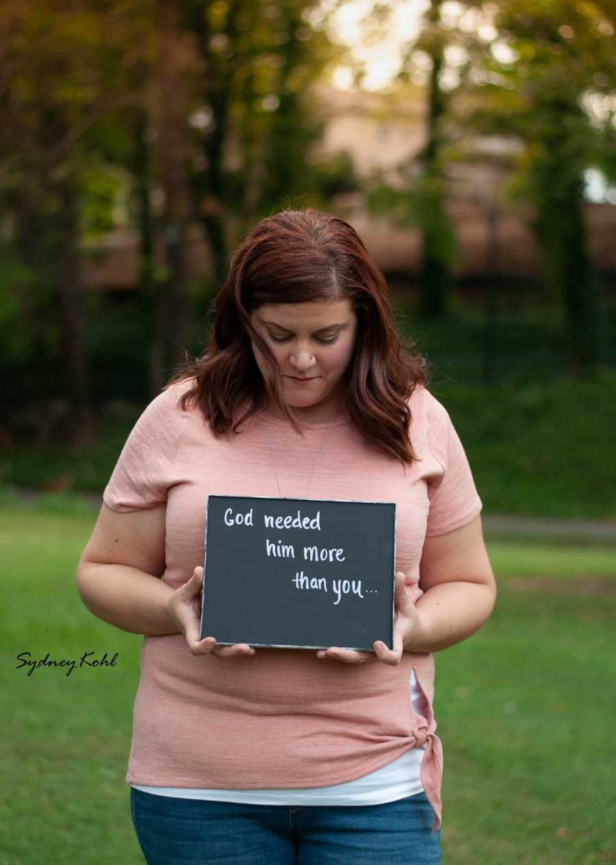 Woman who experienced child loss holds sign that says, "God needed him more than you"