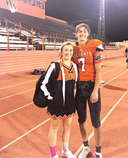 High school football player stands on track smiling with cheerleader girfriend