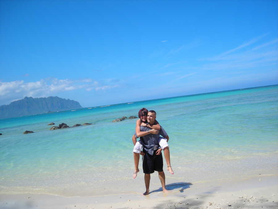 Man stands on shore of ocean with girlfriend on his back