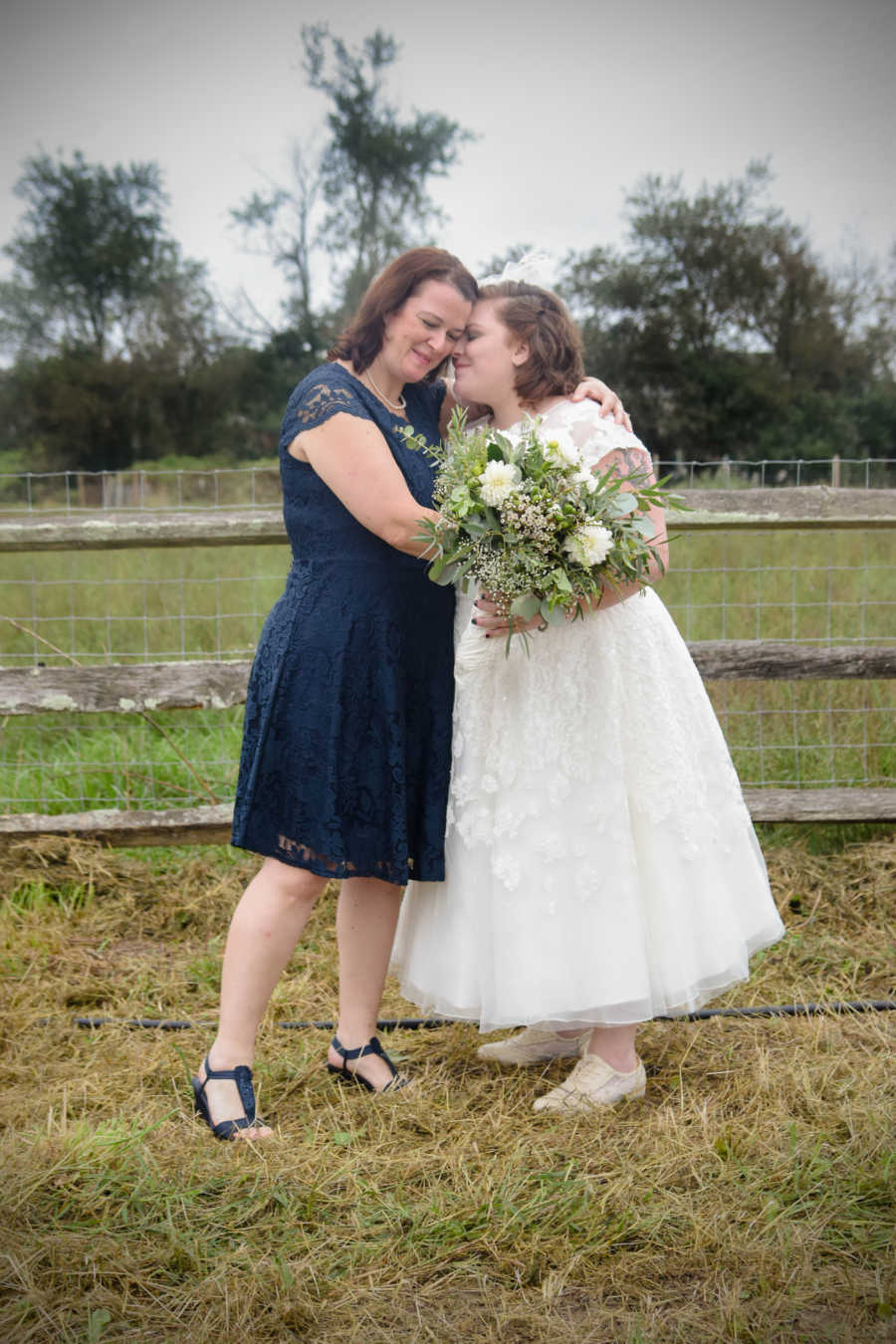 Mother stands outside hugging her daughter she had when she was 18 who is now a bride