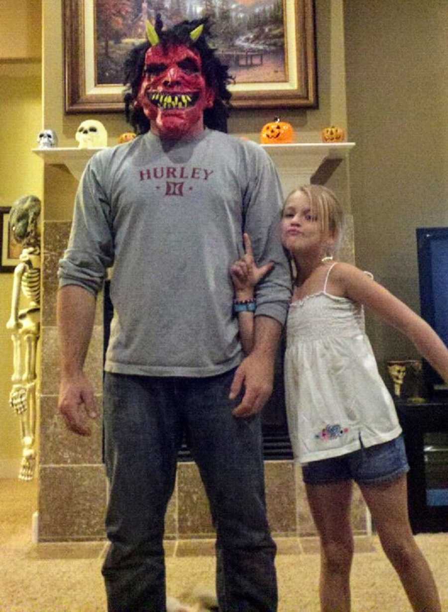 Father who has since passed from pancreatic cancer stands wearing devil mask beside daughter
