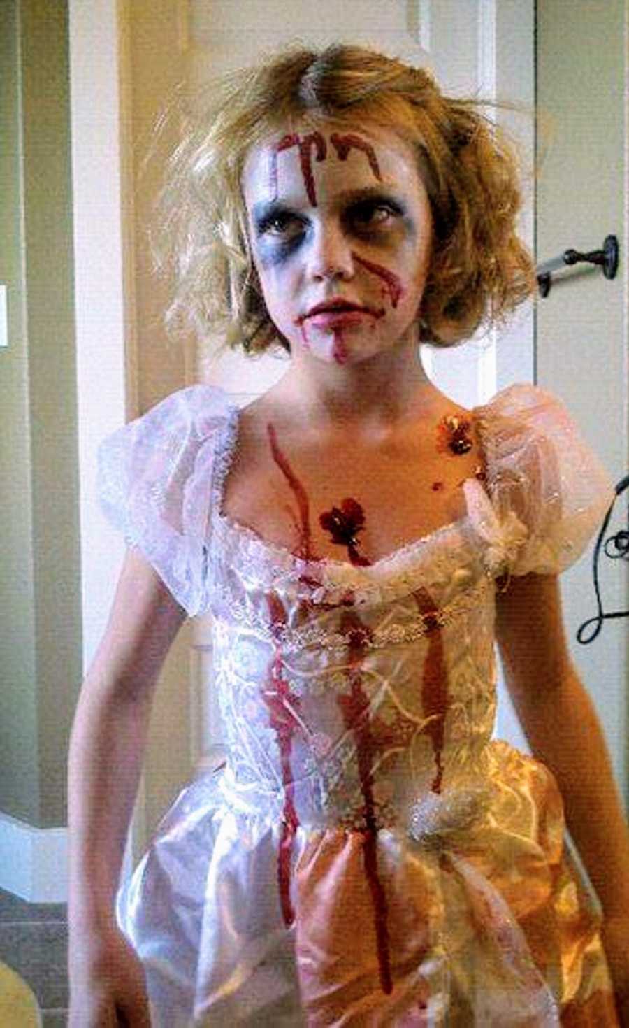 Little girl in white dress stands with fake blood all over her for Halloween