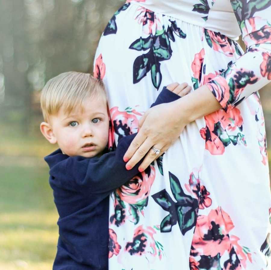 Young boy stands holding stomach of pregnant mother